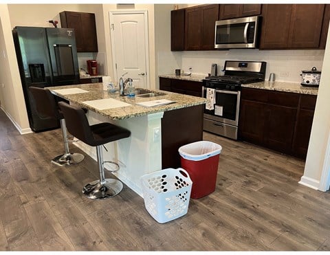 a kitchen with a counter and a bar with chairs and a trash can