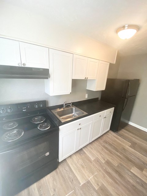 an empty kitchen with white cabinets and a black refrigerator and stove