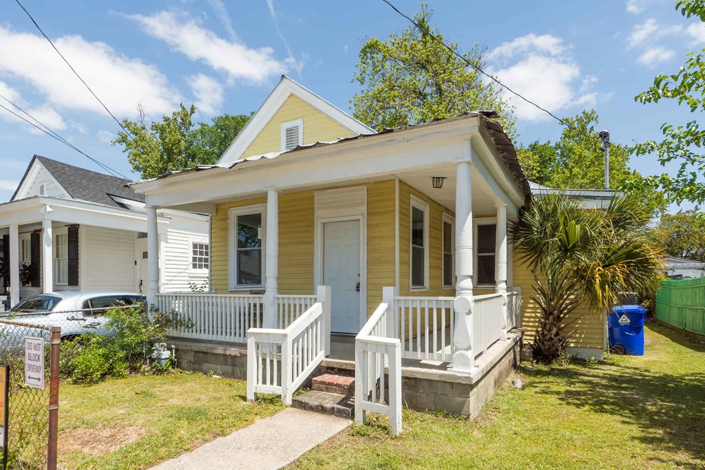 a small yellow house with a porch and a white door