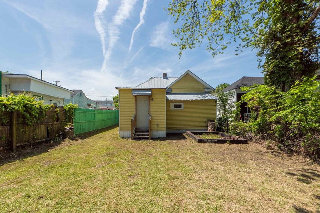 a backyard with a yellow house and a green fence