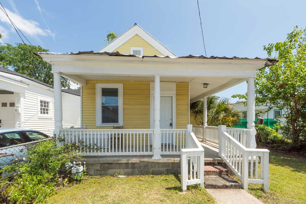 a small yellow house with a porch and a white fence