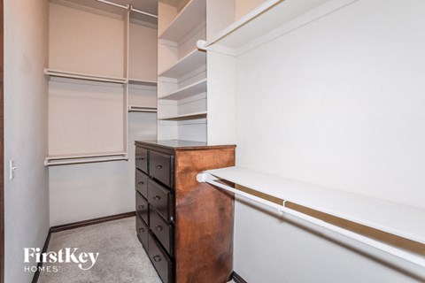 A brown dresser sits in a white room with a white wall and a white closet.