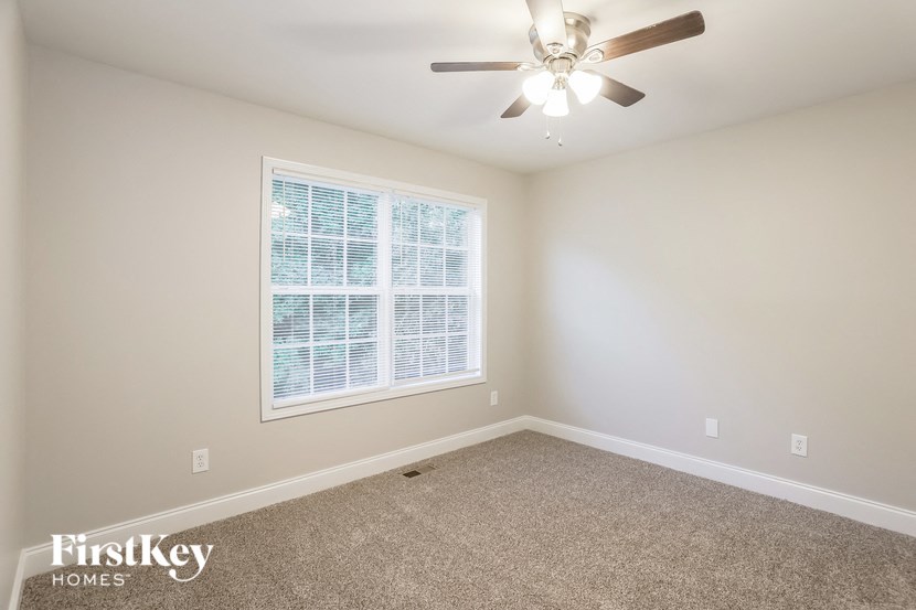 A room with a carpeted floor, a ceiling fan, and a window with blinds.
