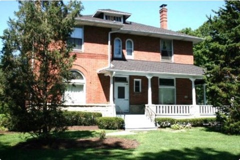 a red brick house with a porch and a tree