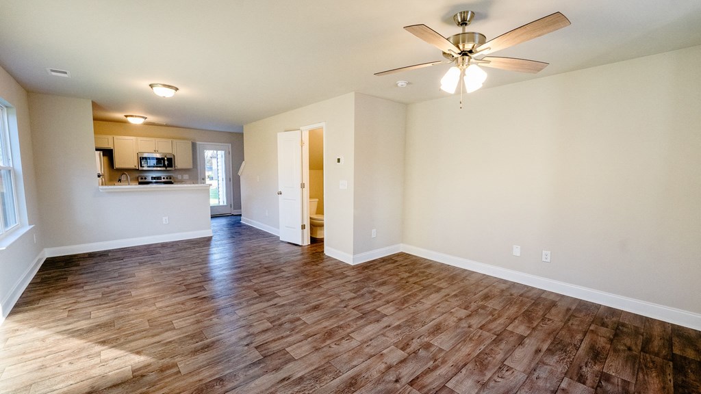 an empty living room with a ceiling fan and a kitchen