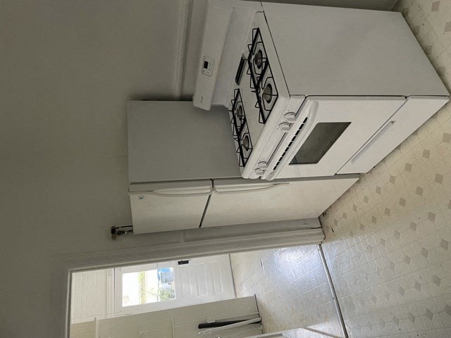 A white stove top oven with four burners and a vent hood above it.