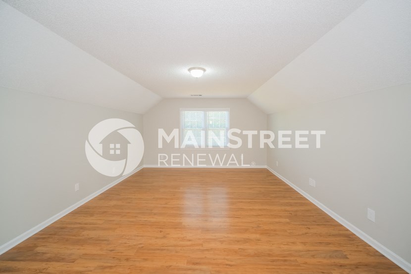 a room with a wood floor and a white wall and a window