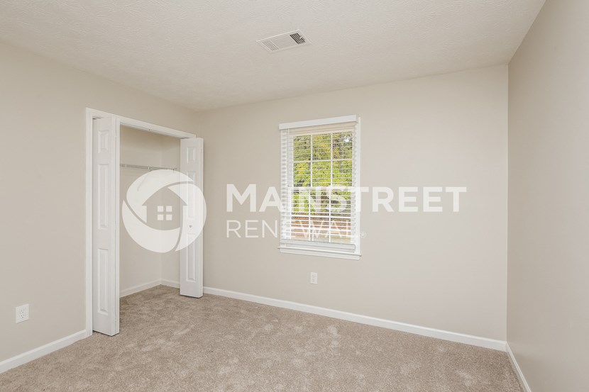 a bedroom with beige carpet and a door to a closet