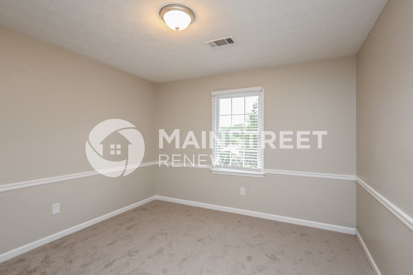 a bedroom with beige walls and carpet and a window