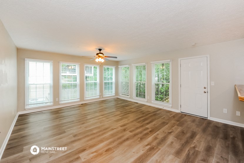 an empty living room with a ceiling fan and windows