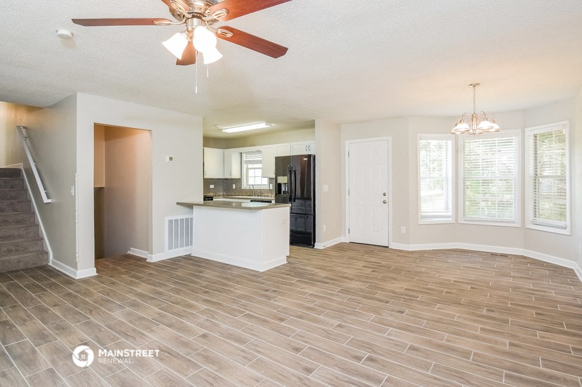 an empty living room with a kitchen and a ceiling fan