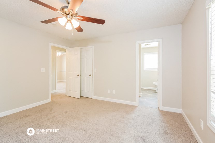 an empty living room with a ceiling fan and a door to a bathroom