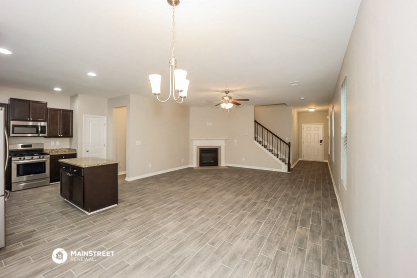 an empty living room with a kitchen and a ceiling fan