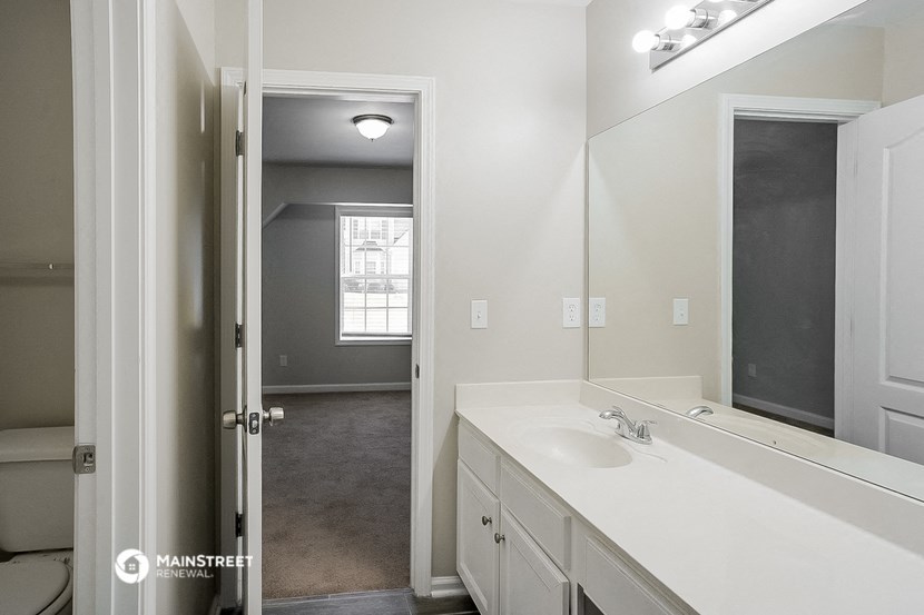 a bathroom with a sink and a mirror and an open door to a bedroom