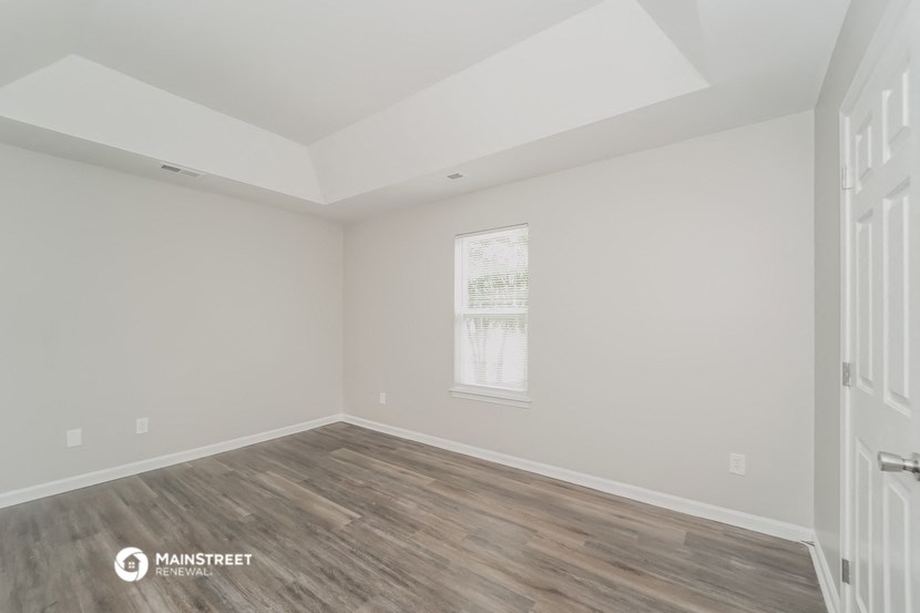a bedroom with white walls and wood floors and a window