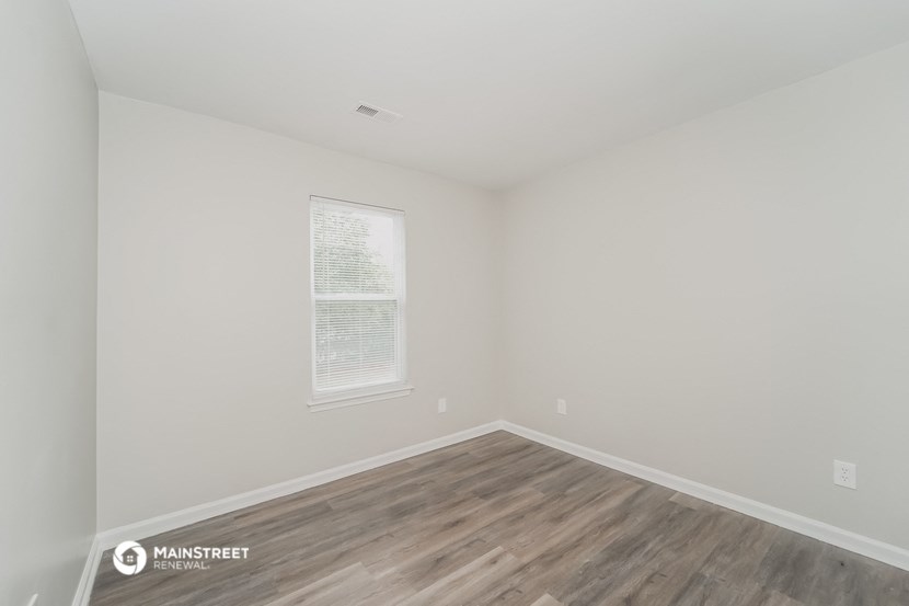 a bedroom with white walls and wood flooring and a window