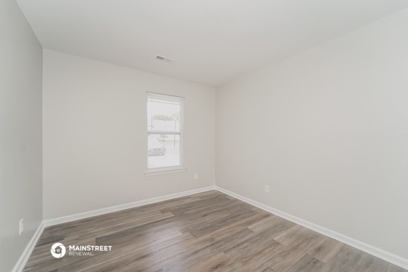 a bedroom with white walls and wood flooring and a window
