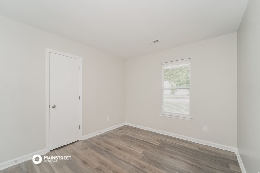 a bedroom with white walls and wooden floors and a window