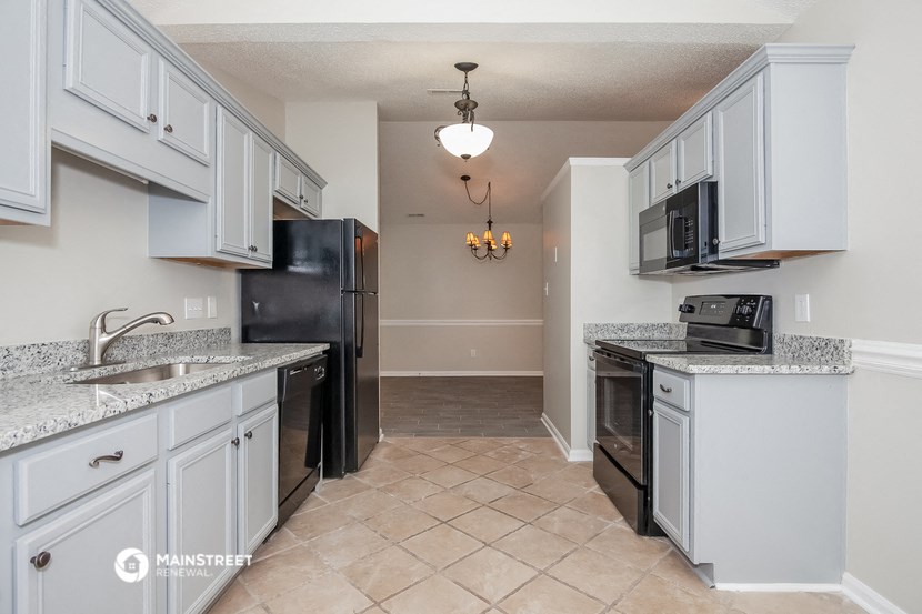 a kitchen with white cabinets and a black refrigerator and a sink