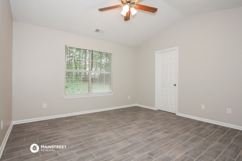 the spacious living room of an empty home with a ceiling fan