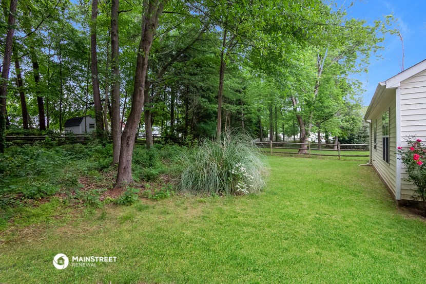 a backyard with green grass and trees and a white house