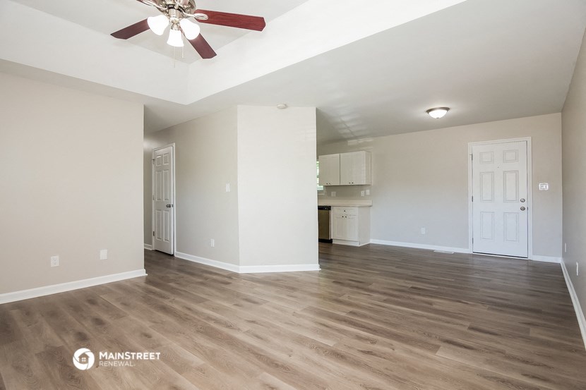 an empty living room with a ceiling fan and a kitchen