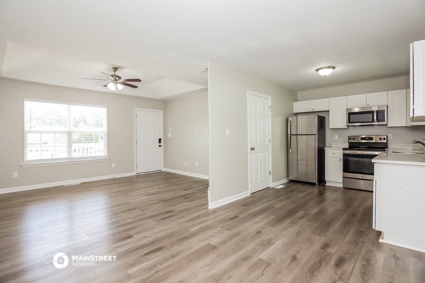 an empty living room with a kitchen and a ceiling fan