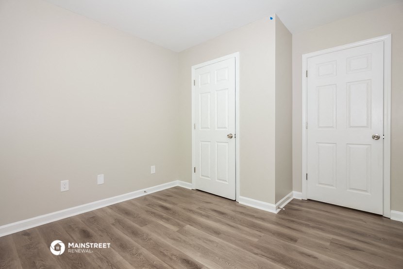 a bedroom with two doors and wood flooring and a closet