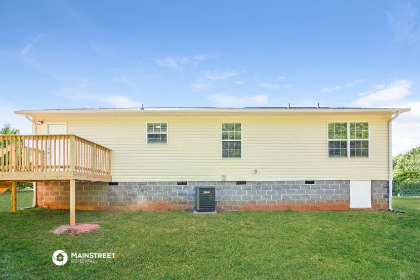 the front of a yellow house with a deck and green grass