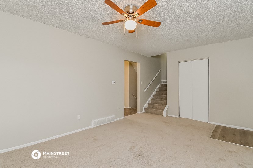 an empty living room with a ceiling fan and a door to a staircase