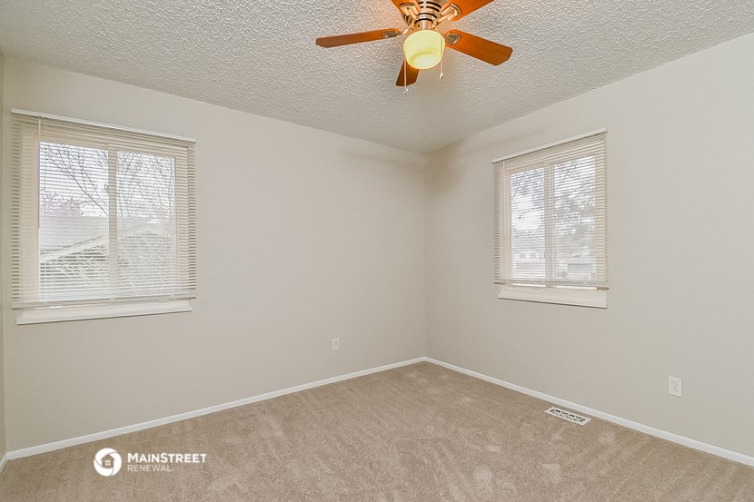 a bedroom with a ceiling fan and two windows