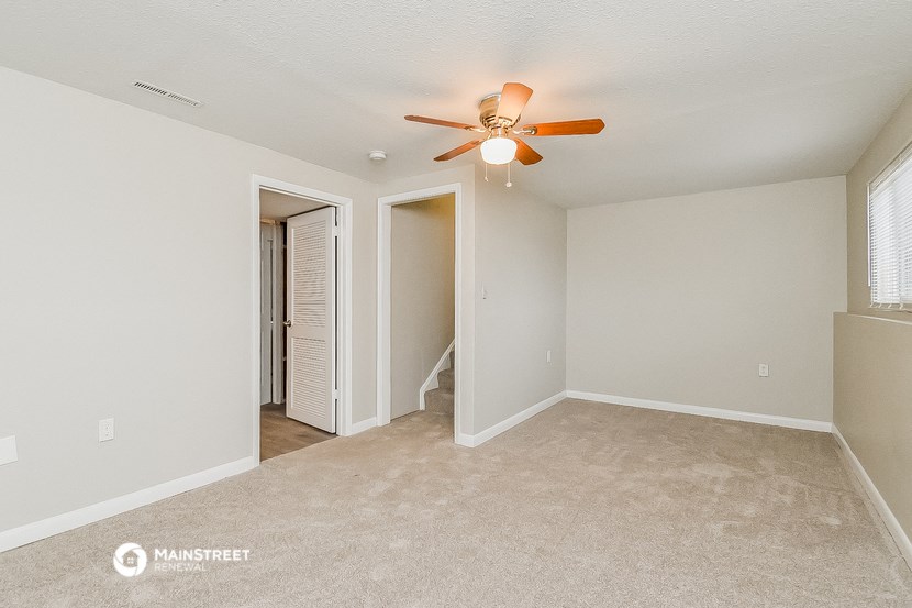 an empty living room with a ceiling fan and a door to a closet