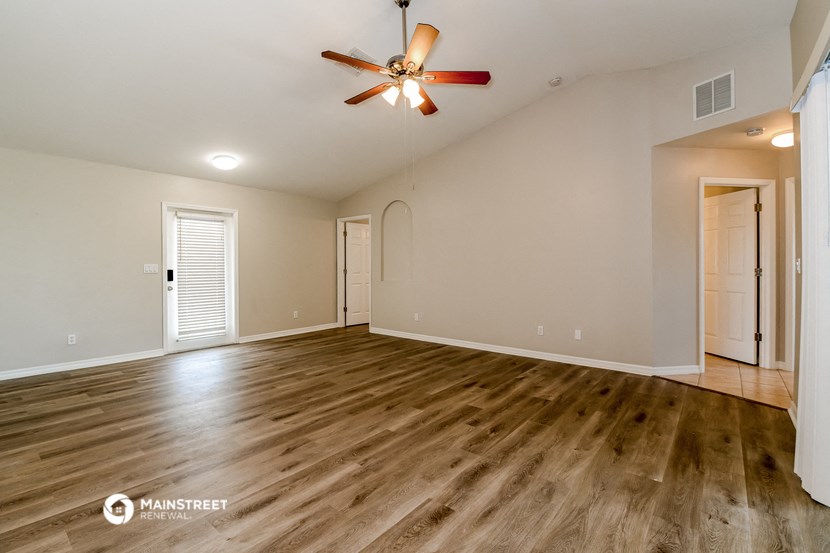 the spacious living room with hardwood floors and a ceiling fan