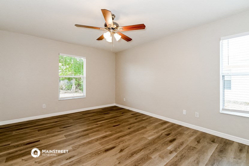 the spacious living room with wood flooring and a ceiling fan