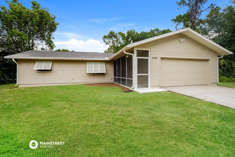 the front of a tan house with a lawn and a driveway