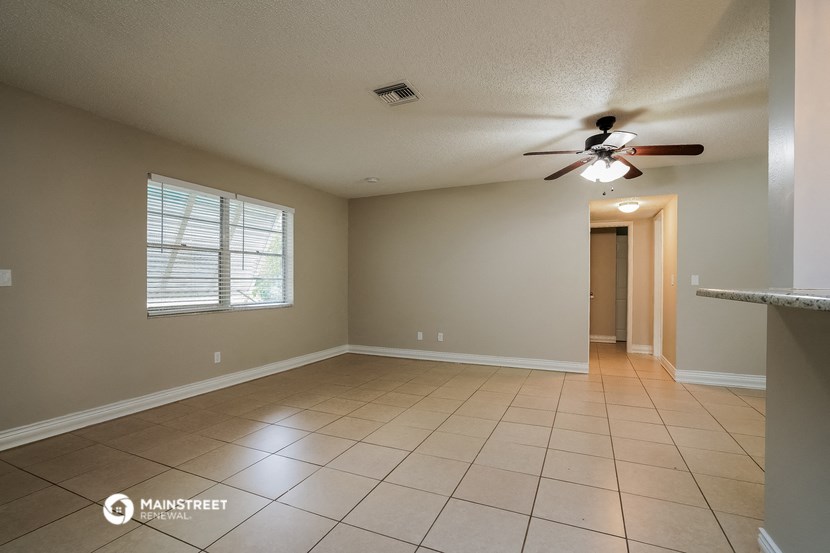 an empty living room with a ceiling fan and tiled floors