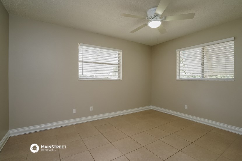 an empty room with a ceiling fan and two windows