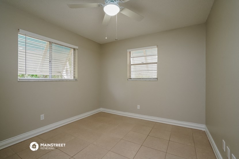 the spacious living room with two windows and a ceiling fan