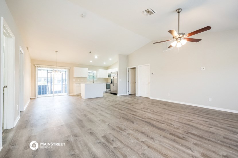 an empty living room with a ceiling fan and a kitchen