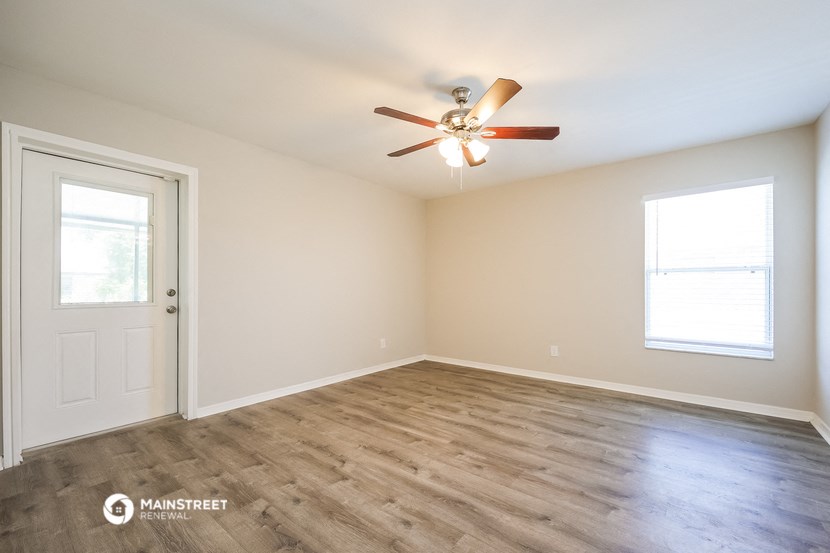 the spacious living room with wood flooring and a ceiling fan