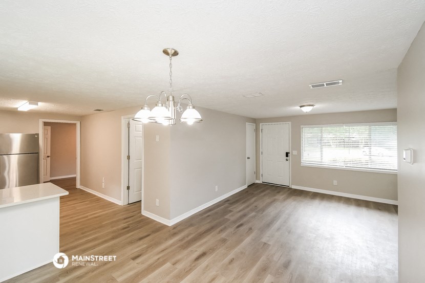an empty living room and kitchen with wood flooring and white walls