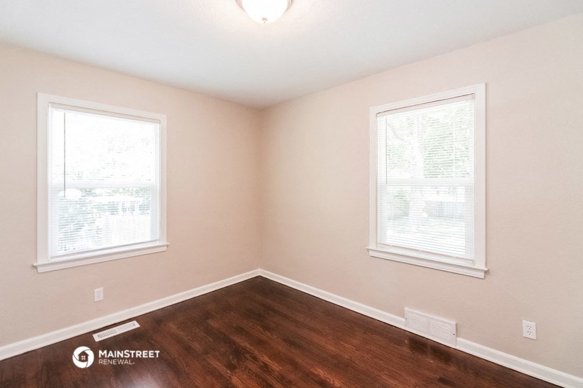 the interior of a bedroom with wood flooring and two windows