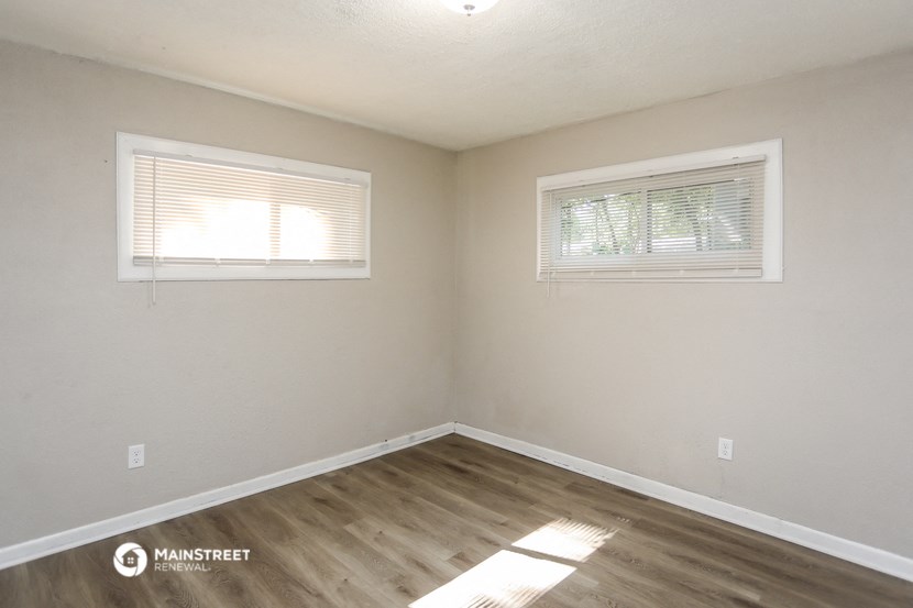the interior of a white room with wooden floors and two windows