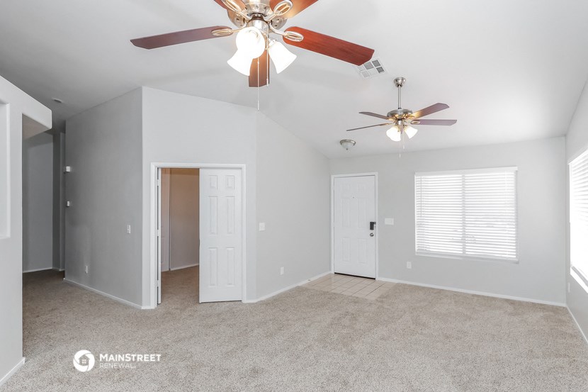 the spacious living room with ceiling fans and white walls