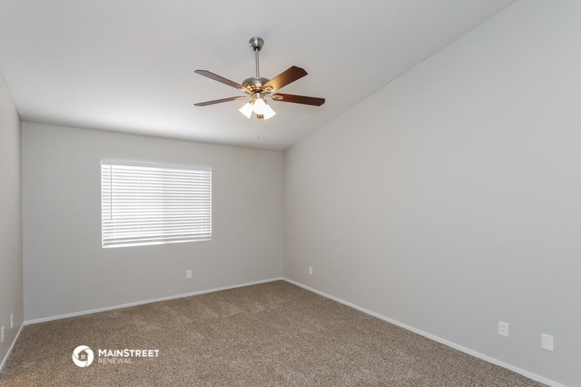 the bedroom has a ceiling fan and a carpet