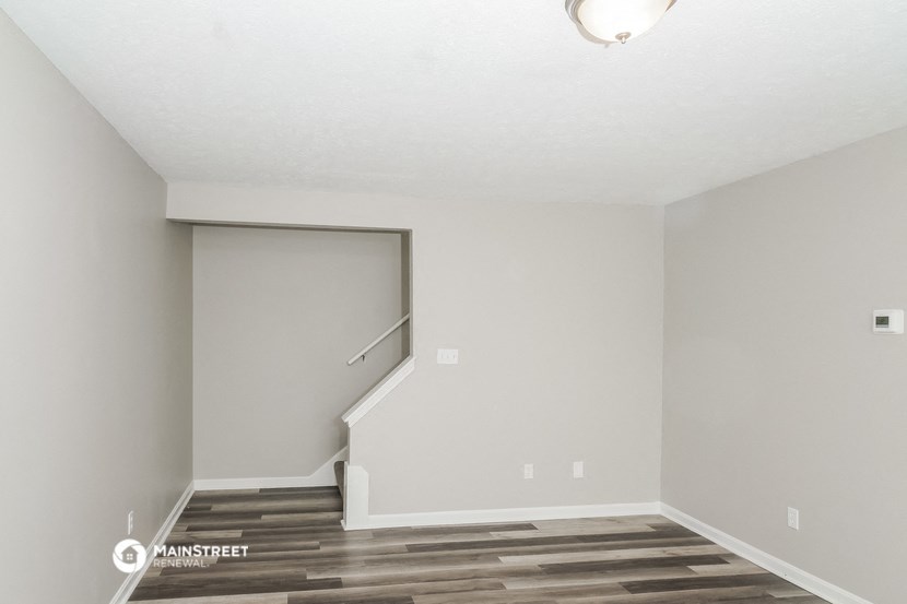 the living room of an apartment with a hardwood floor and a staircase