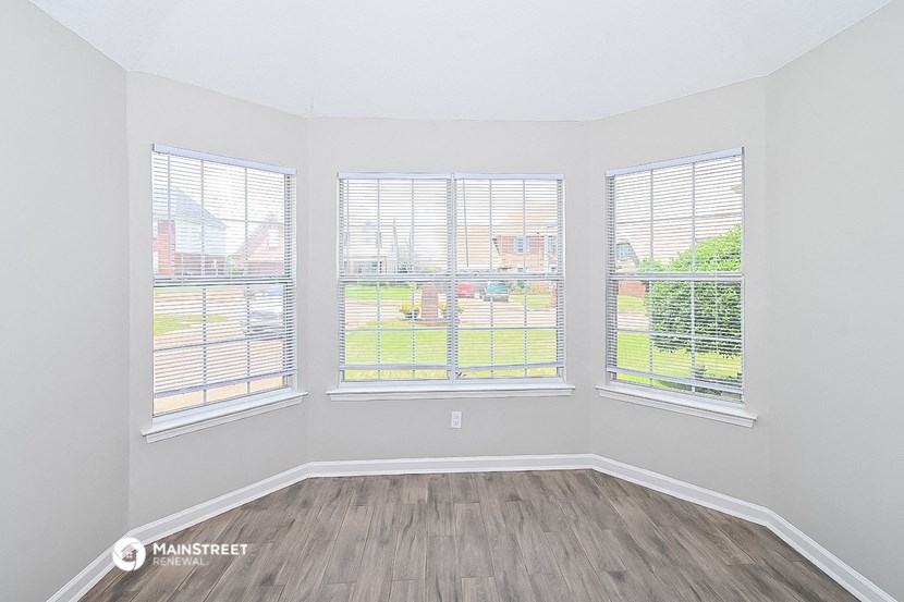 the spacious living room with three windows and wood flooring