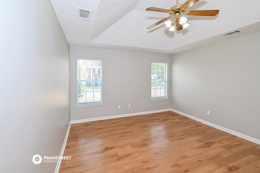 the spacious living room with hardwood flooring and a ceiling fan