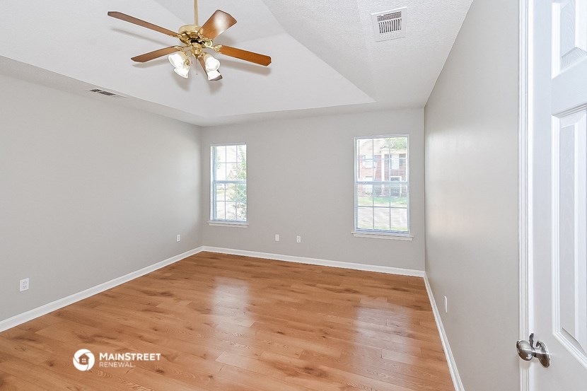 the spacious living room with hardwood flooring and a ceiling fan