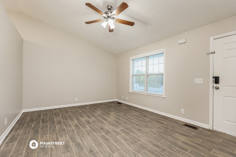 the spacious living room with wood flooring and a ceiling fan